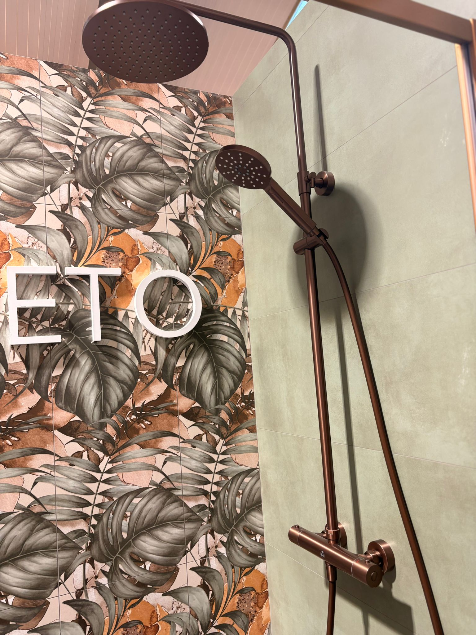 Copper shower set against a botanical tile wall in the showroom