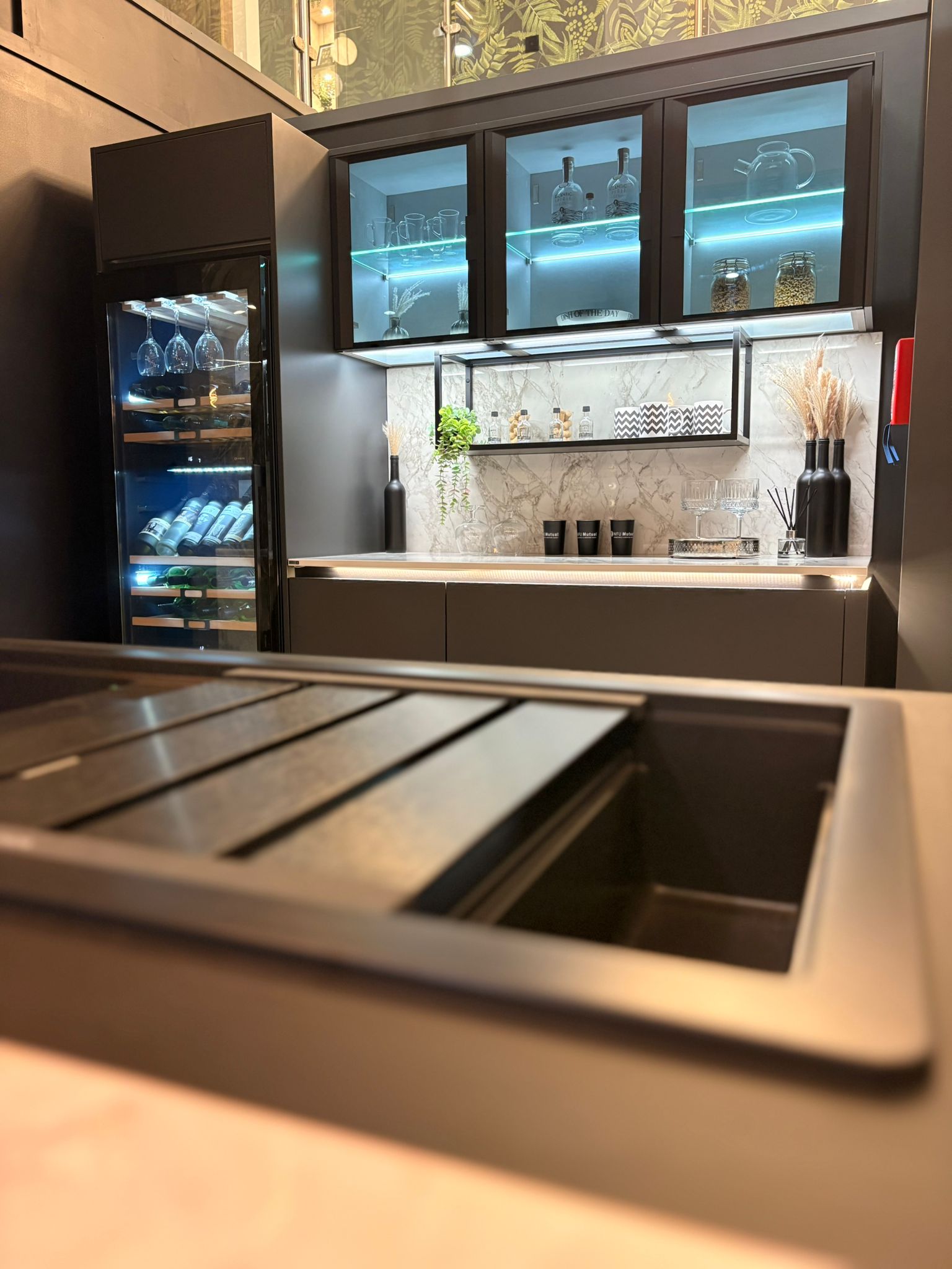 Showroom kitchen display with glass-fronted wall cabinets and a wine cooler