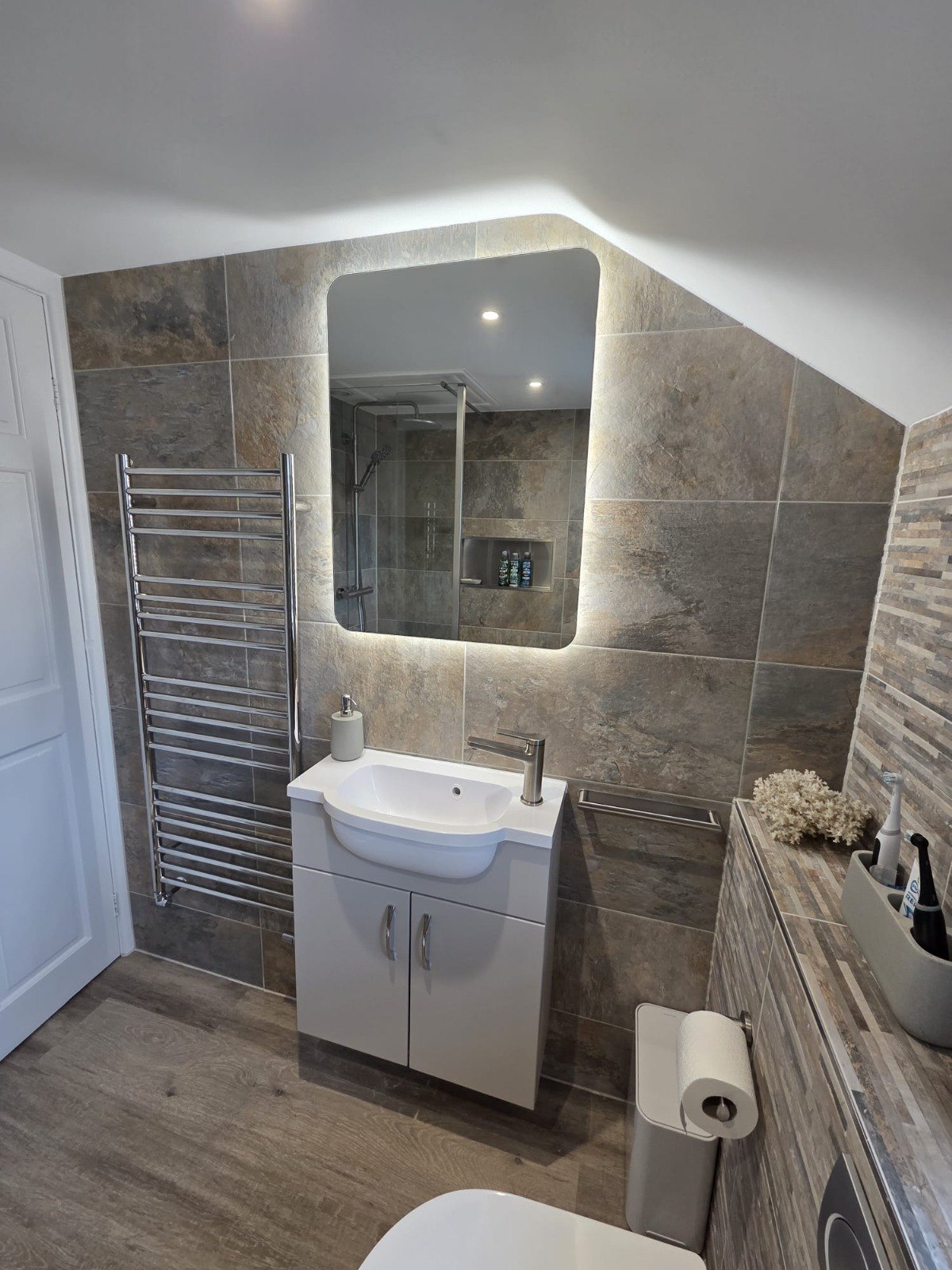Grey tiled bathroom with a backlit mirror and vanity unit