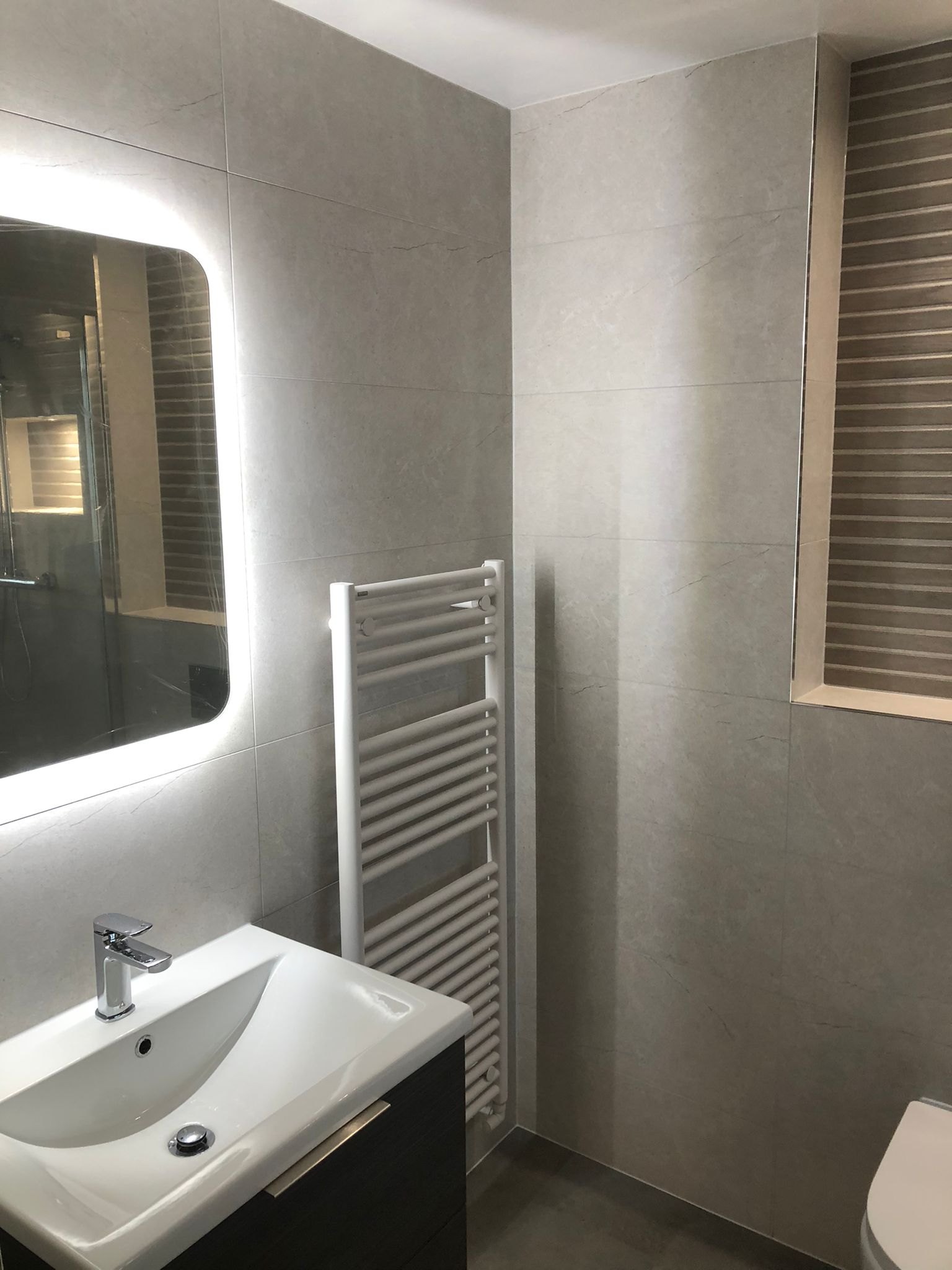 Bathroom basin and illuminated mirror with a white towel rail