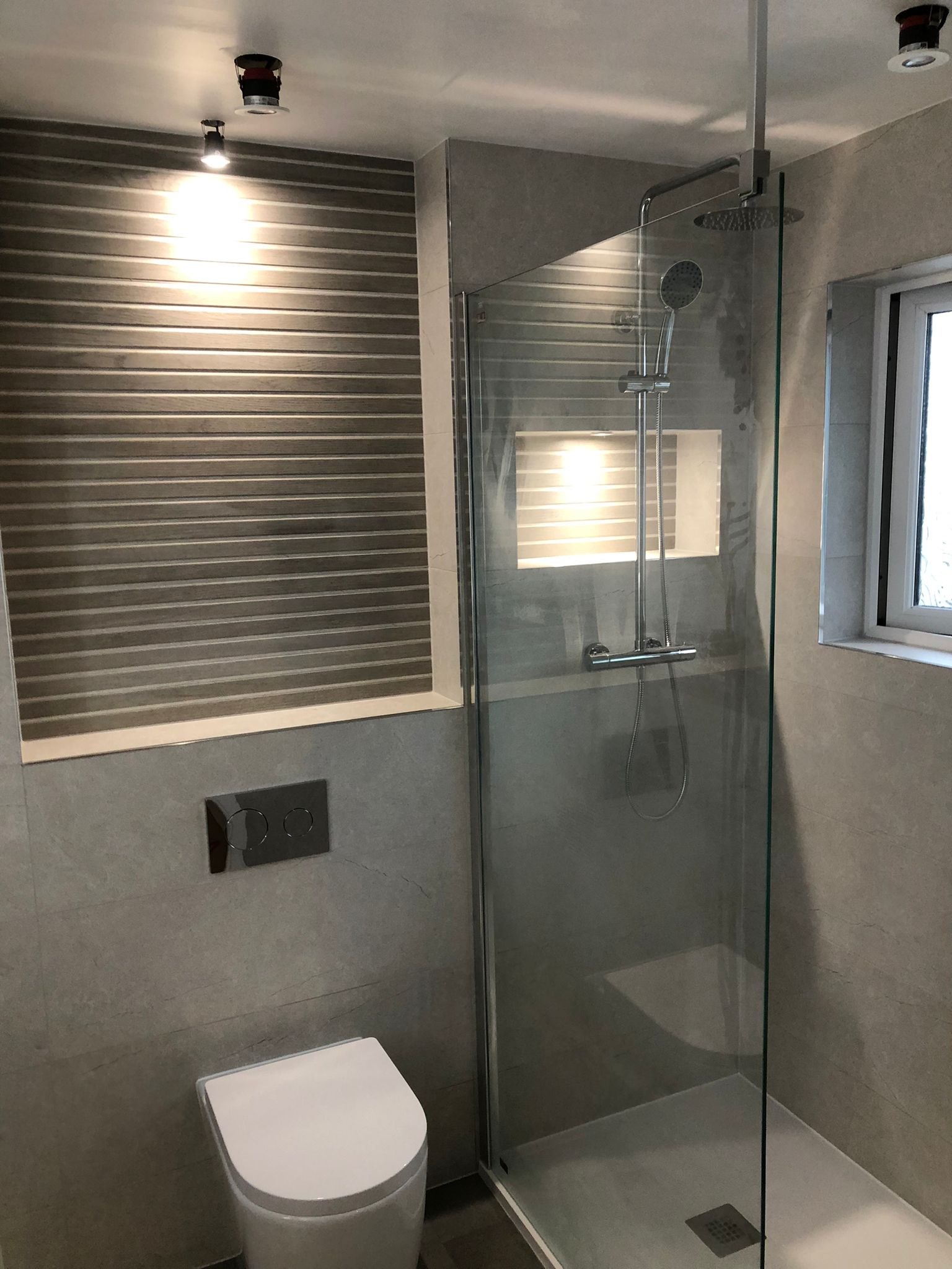 Walk-in shower with a glass screen and grey tiling