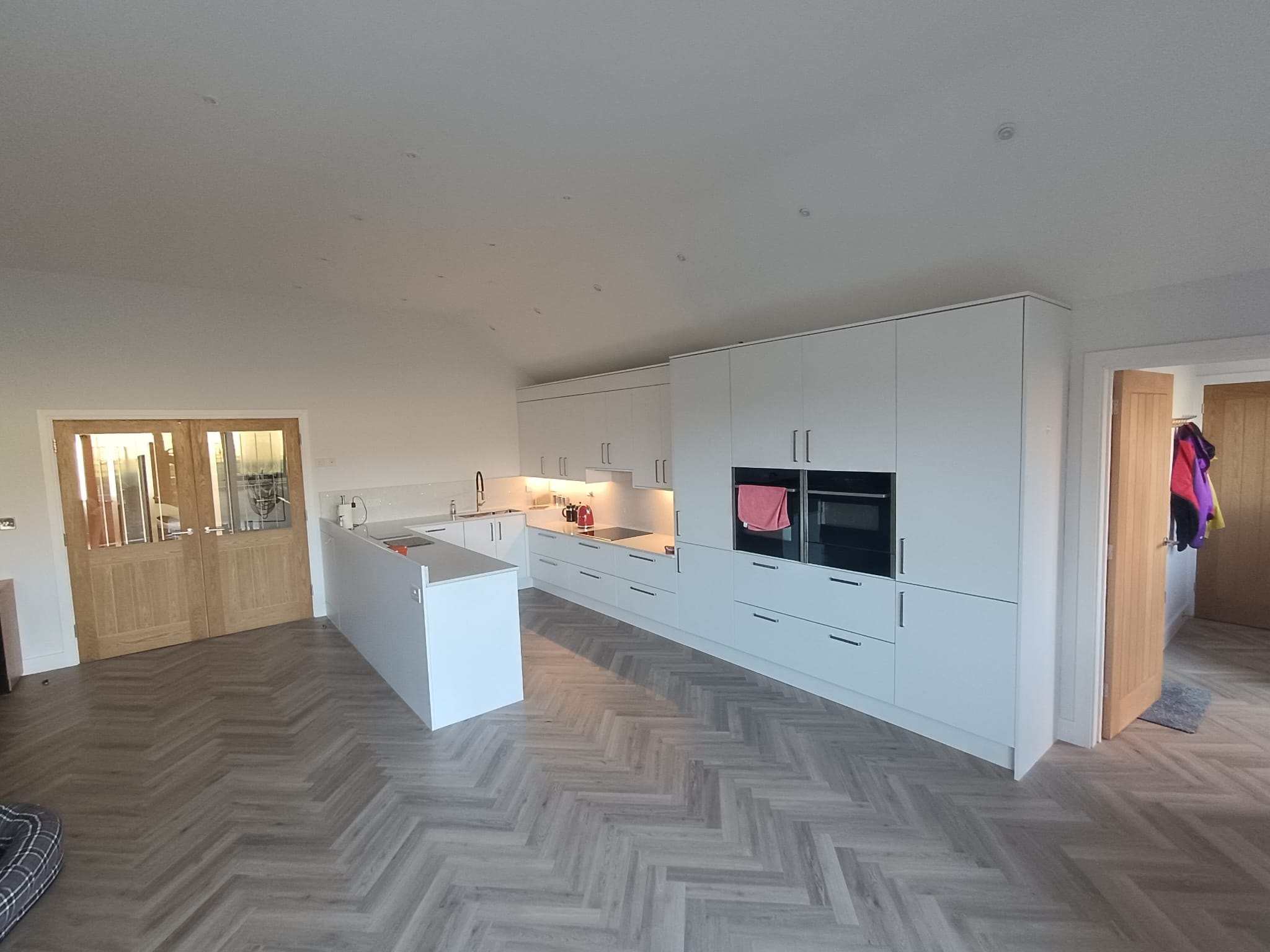 White handleless kitchen with tall units and herringbone flooring